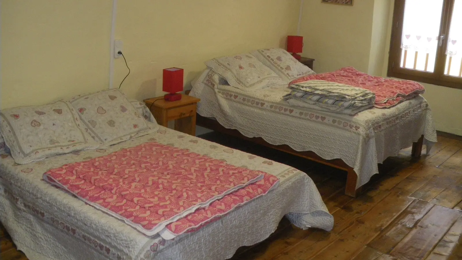 Chambre à coucher lumineuse avec deux lits doubles, ameublement bois, parquet au sol, fenêtre