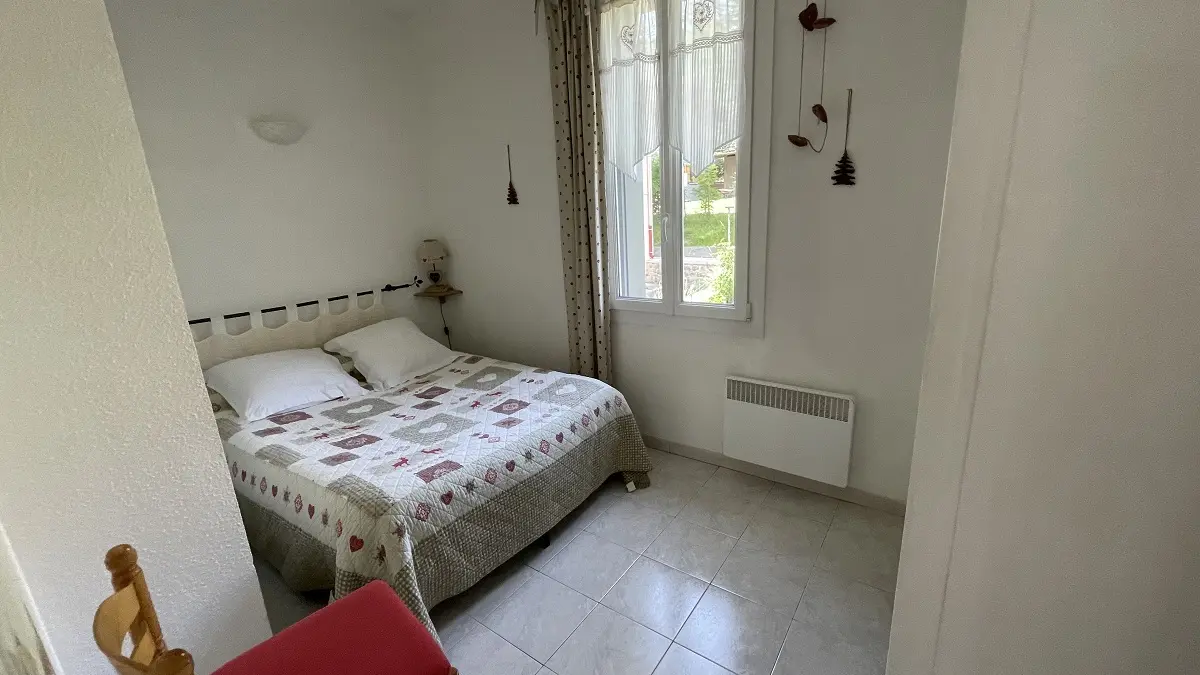 Chambre à coucher lumineuse avec lit double, sol carrelé, ameublement bois