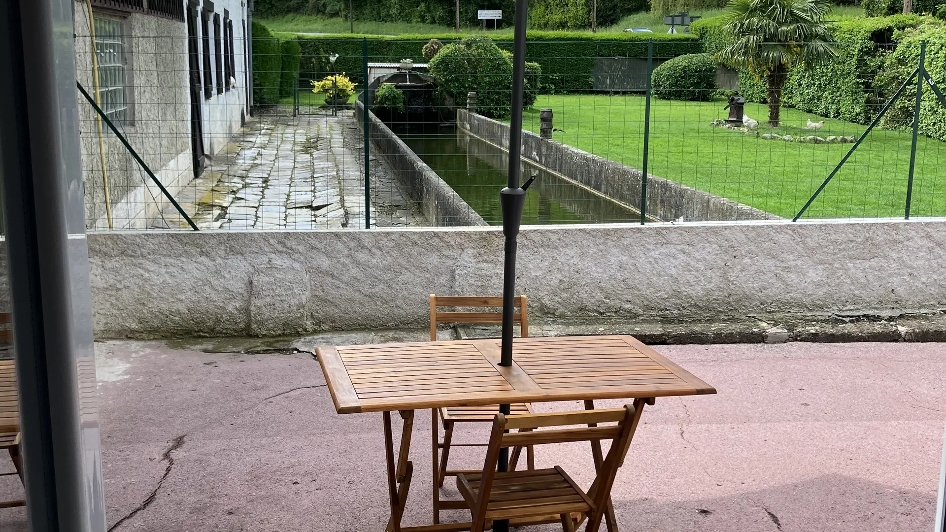 La terrasse est équipée d'un parasol, d'une table et d'une chaise. Le sol est dur et plat.