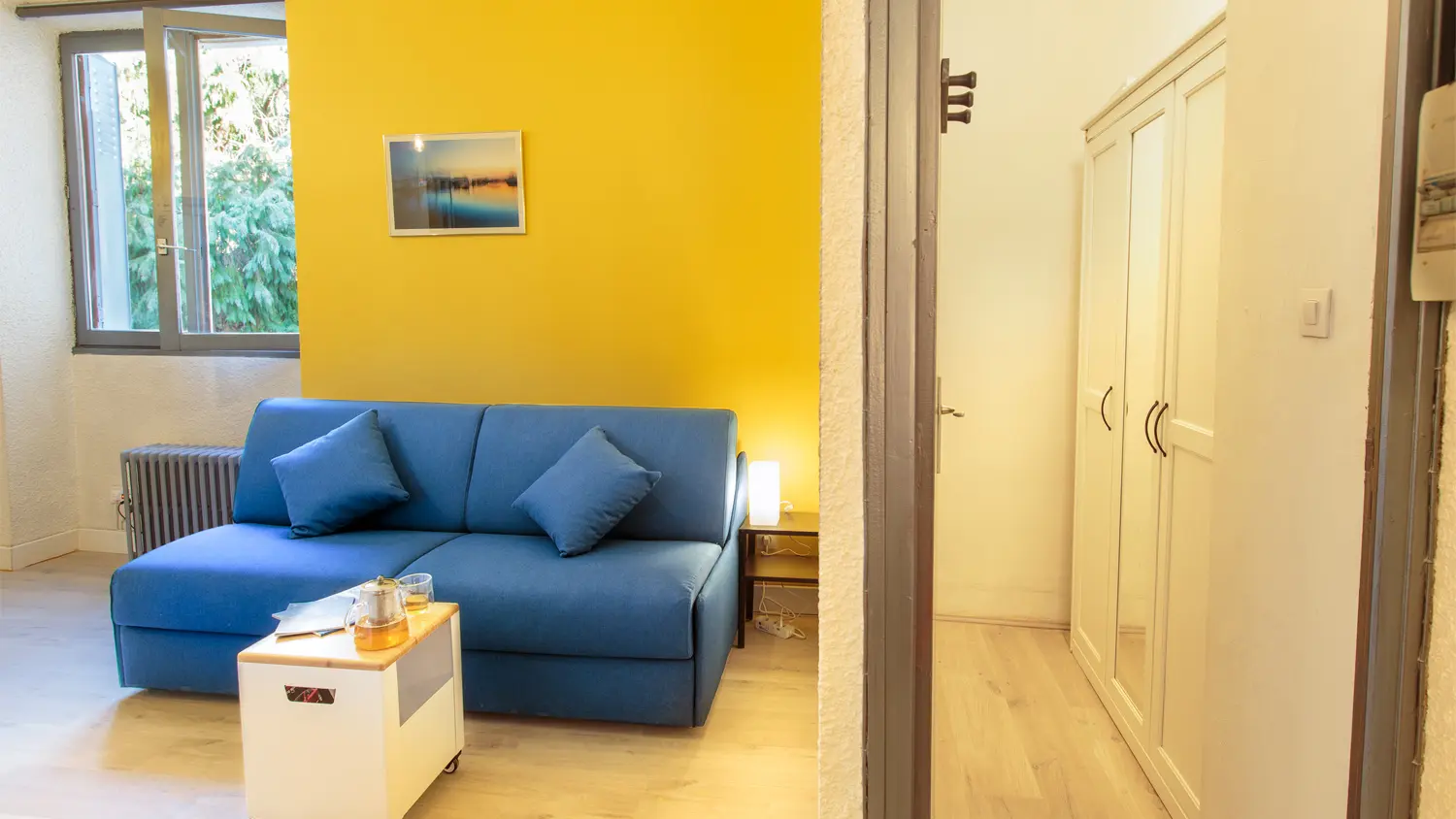 Un salon lumineux et accueillant avec un canapé bleu marine et un mur jaune vif, offre un espace de détente agréable.