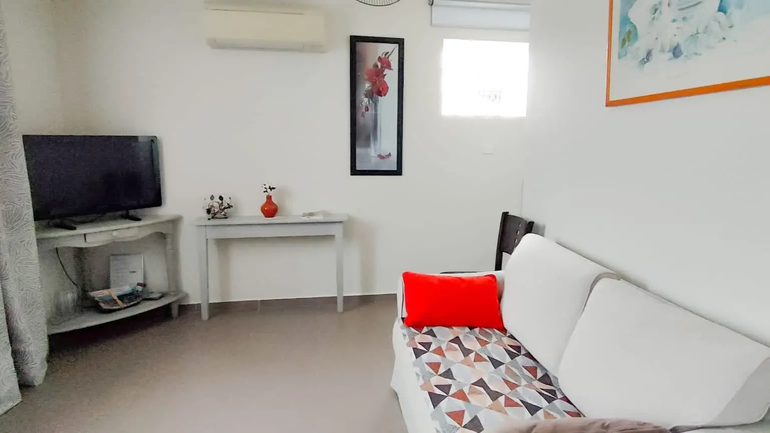 Espace salon agréable avec canapé, télévision et décoration moderne aux tons clairs.