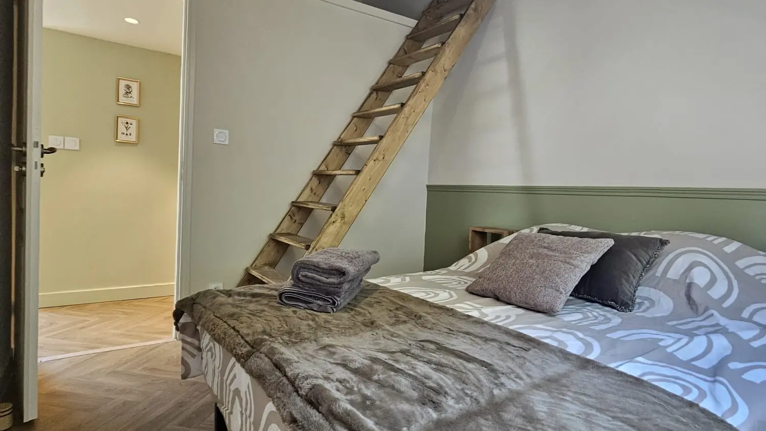 Une chambre sous les combles dotée de poutres apparentes au plafond, où se trouve un lit double.