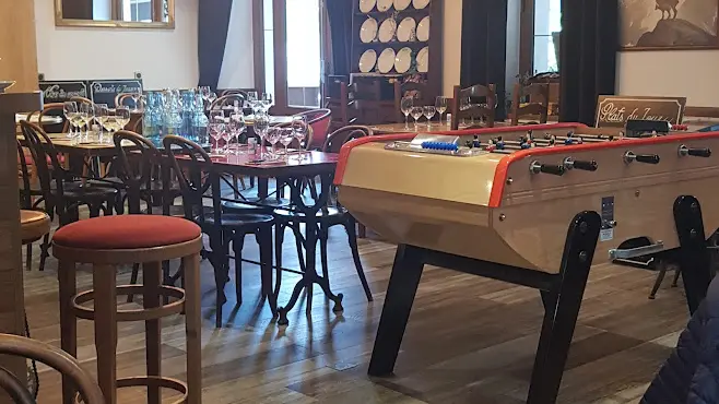 Salle de restauration avec des tables, chaises et tabourets en bois avec un baby-foot.