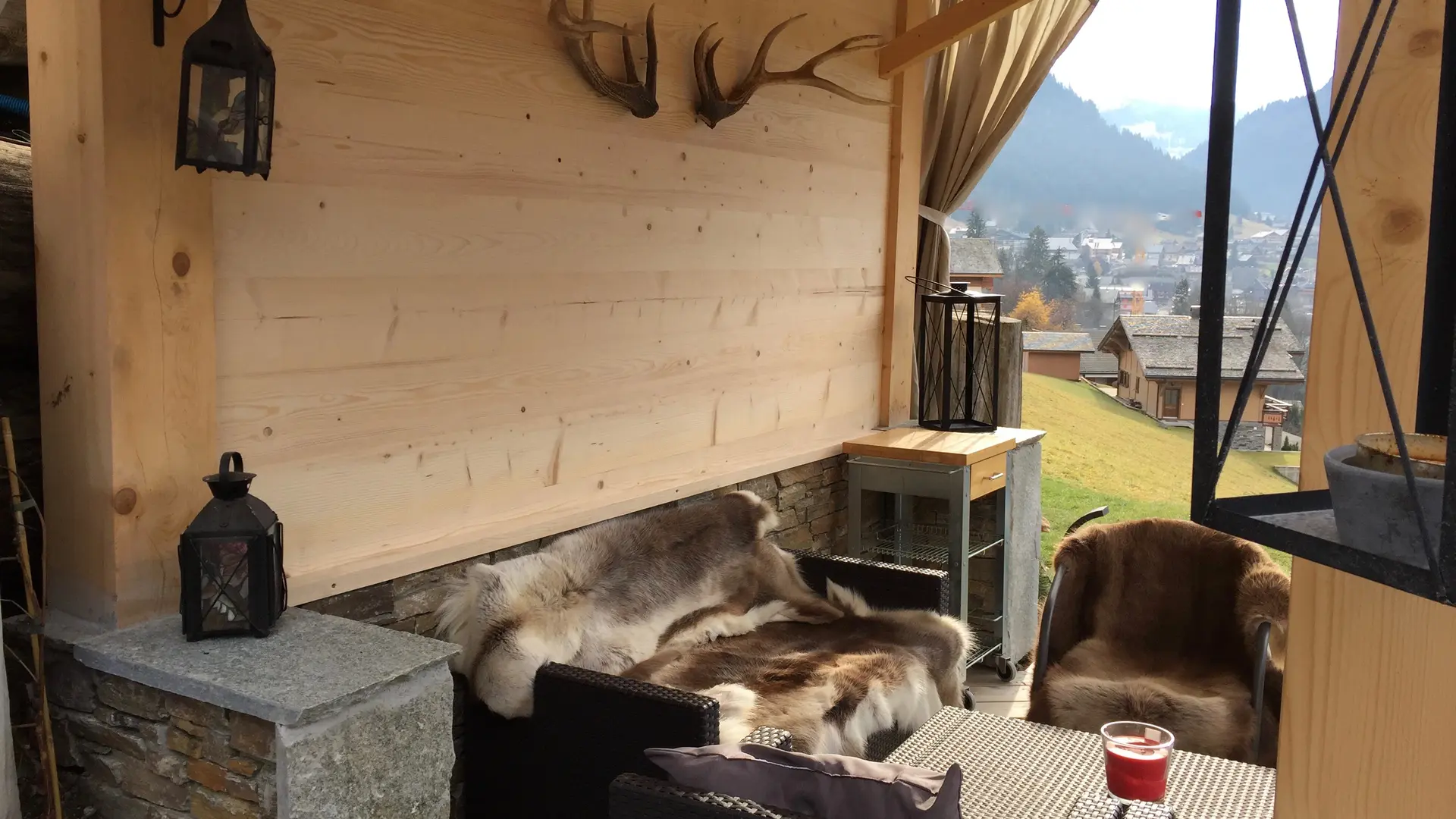 Coin détente extérieur abrité avec canapé et fauteuils, vue sur le village
