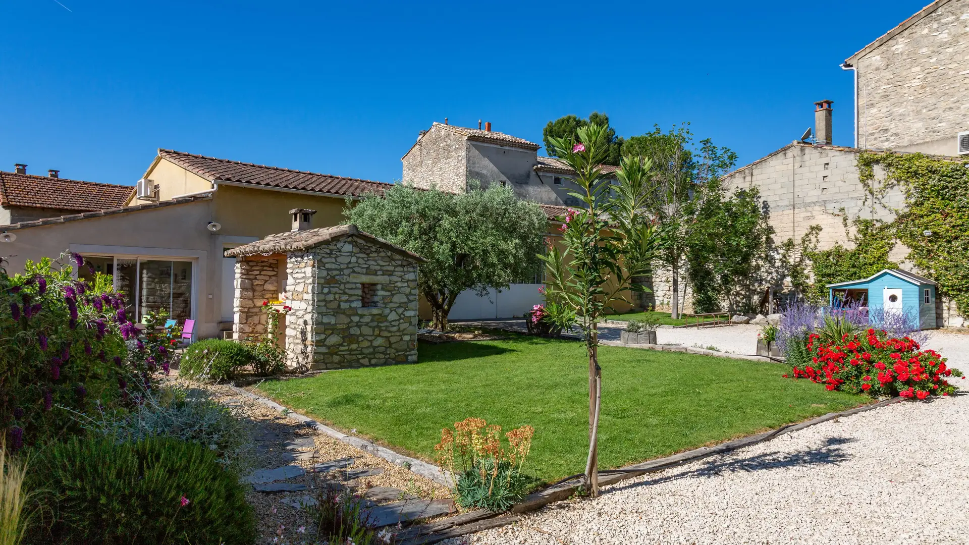 Un vaste jardin soigneusement entretenu, mêlant pelouse, massifs fleuris et bâtisses en pierre, offrant un cLe jardin s’illumine à la tombée de la nuit, créant une atmosphère douce et conviviale pour profiter des soirées d’été en toute tranquillité.