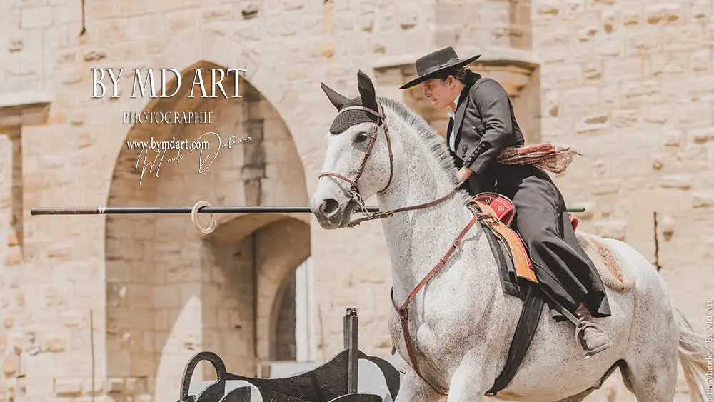 Cavalière en tenue traditionnelle exécutant une épreuve équestre devant une bâtisse en pierre.