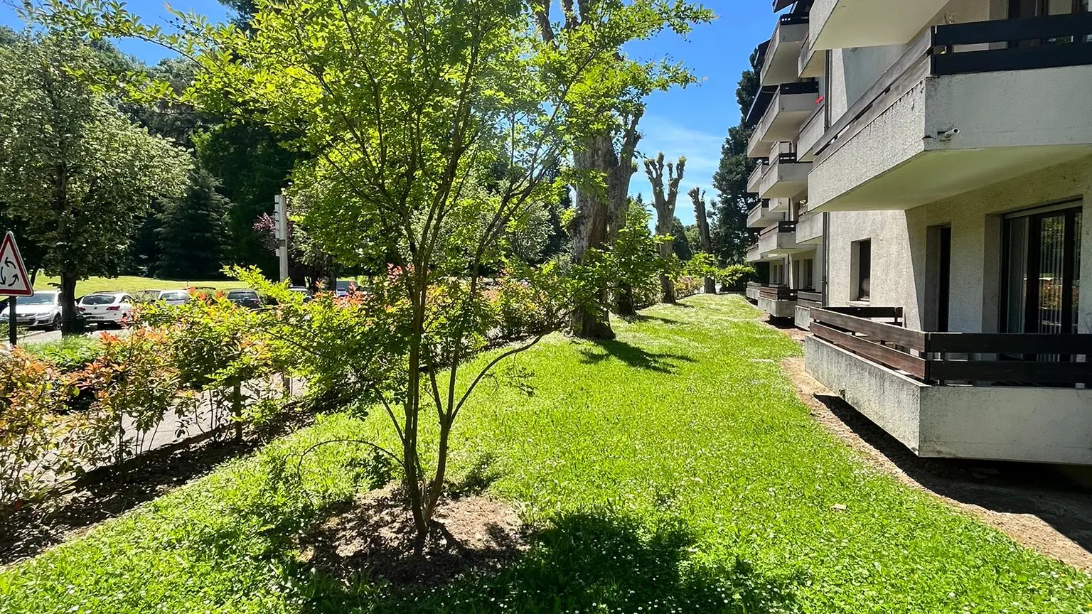 Un grand immeuble moderne avec une façade claire et de nombreux balcons et fenêtres est visible sur le côté droit, s'étendant dans le sens de la longueur à travers l'image.