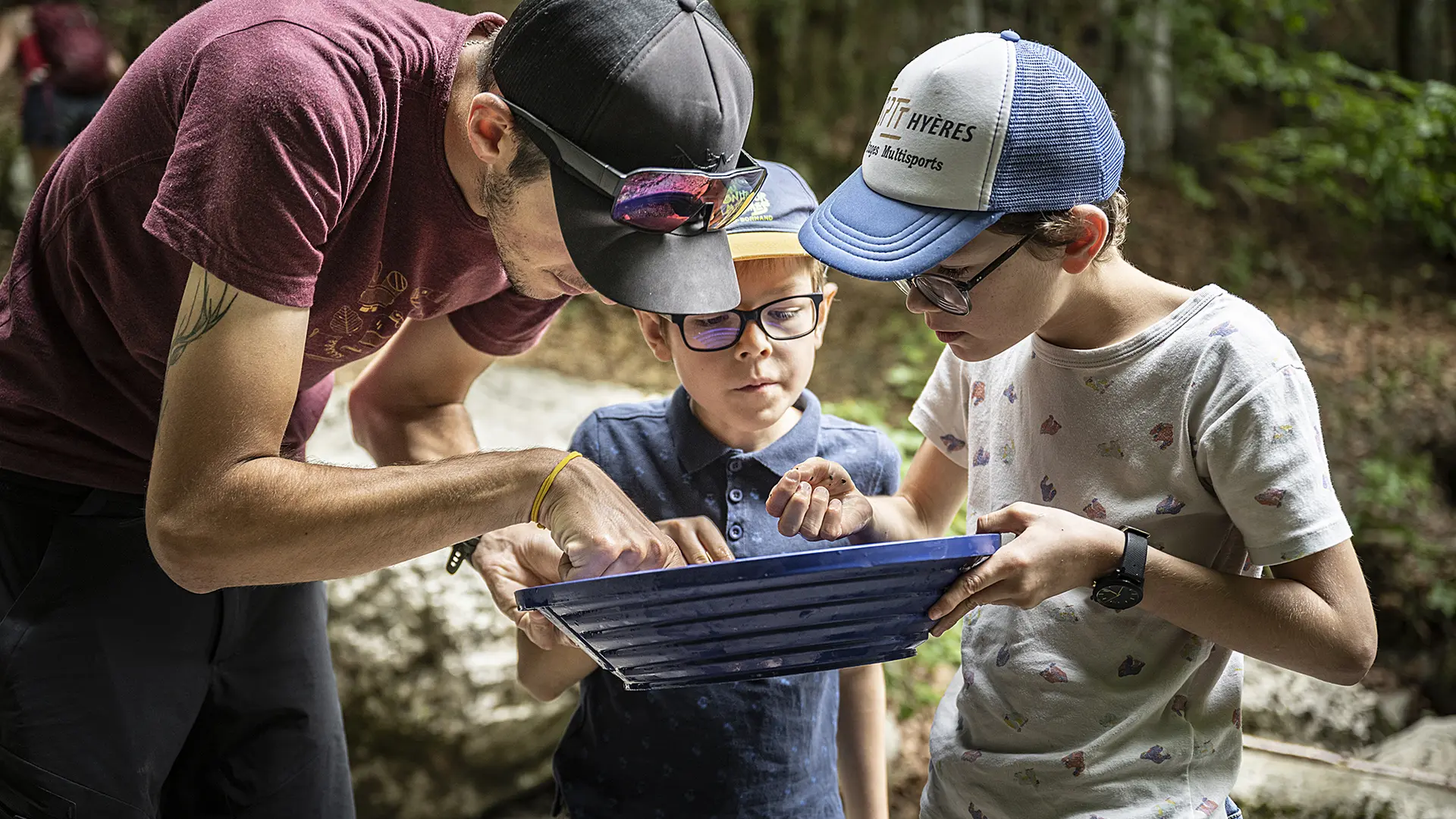 2 enfants et un adulte regardent dans le tamis à la recherche de pépites d'or