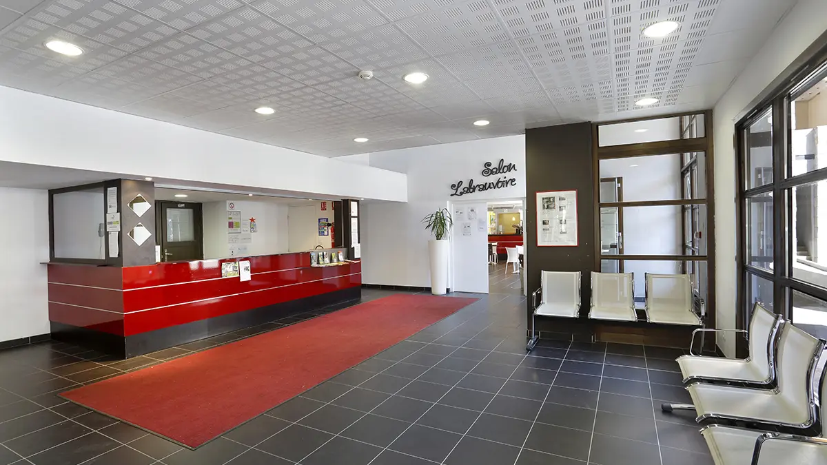 Réception de la résidence, carrelage au sol, comptoir d'accueil, chaises pour l'attente, porte vers salon