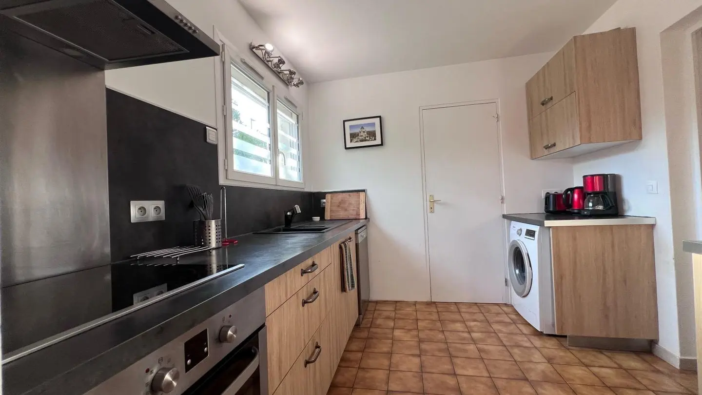 Cuisine équipée : Four, plaque à induction, hotte aspirante, lave-vaisselle, lave-linge, bouilloire, micro onde, sèche-linge, frigo avec congélateur, vue sur le jardin.