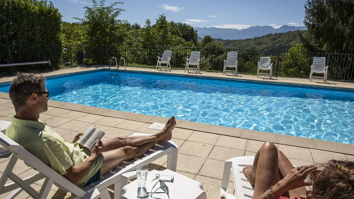 Deux personnes sont allongées sur des chaises longues en plastique, les pieds posés sur le bord d'une piscine rectangulaire.