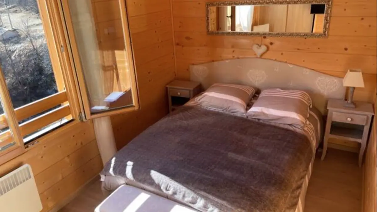 Bright bedroom with wooden furniture, panelling, double bed with mirror, curtains, unobstructed view of the mountains from window