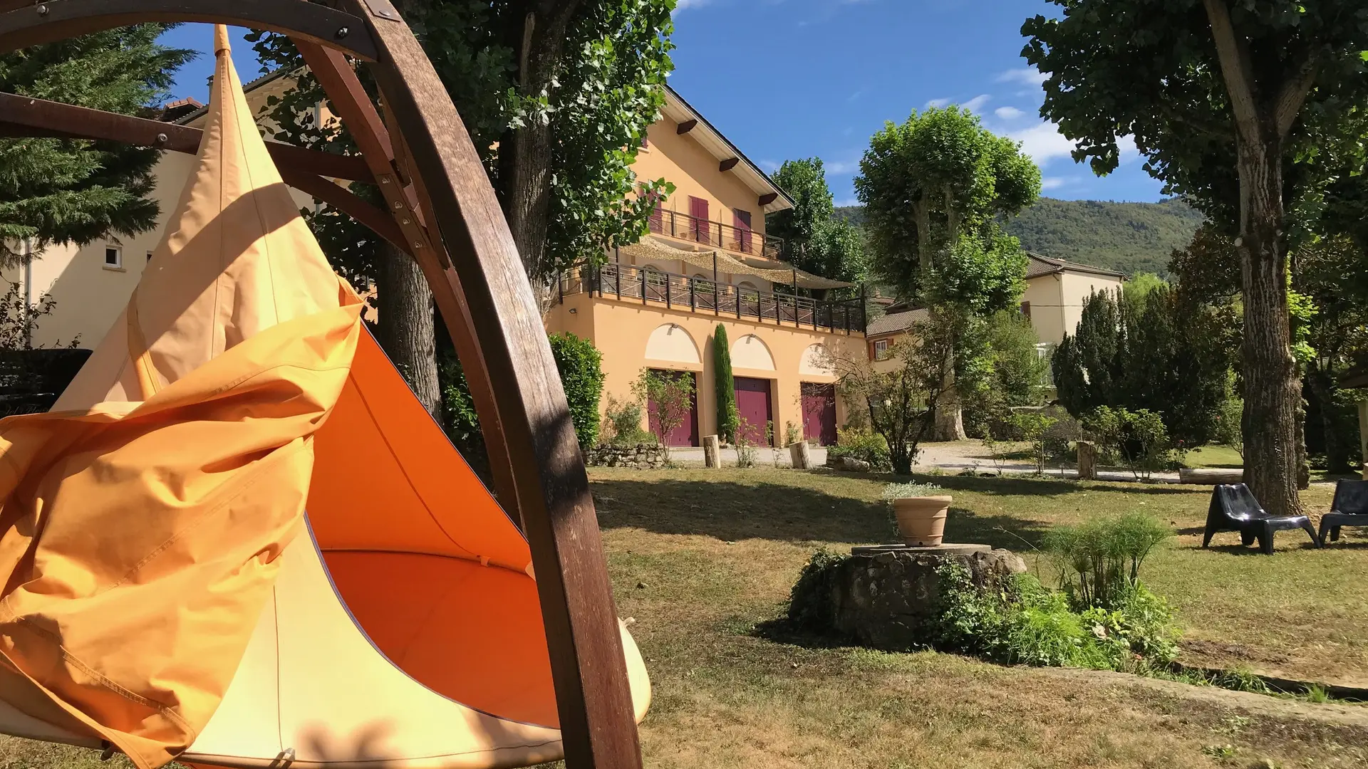 Tipi installé dans un jardin baigné de lumière avec assises et entouré de végétation