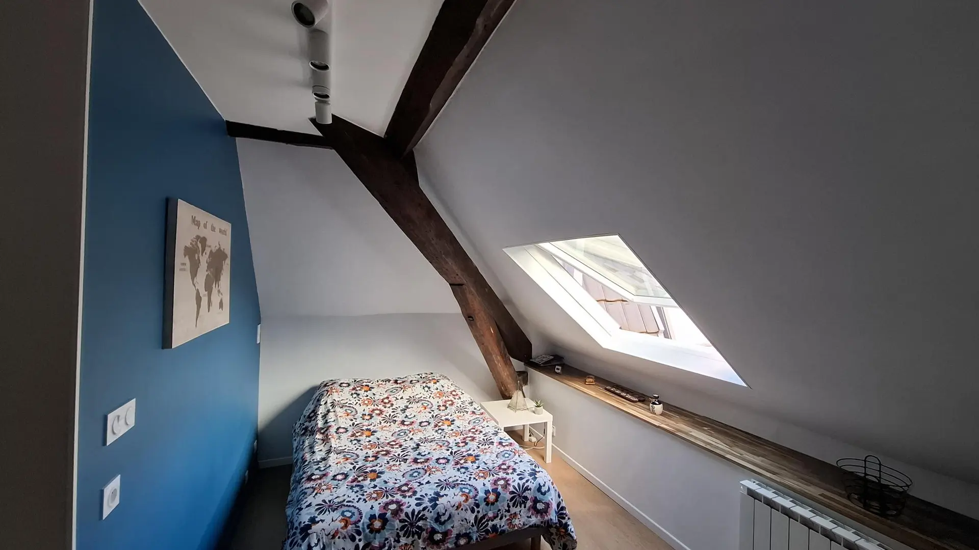 Sous une charpente en bois apparente, ce studio mansardé est aménagé avec un lit double recouvert d'une couette. Un velux apporte de la lumière naturelle et donne une vue sur le ciel.