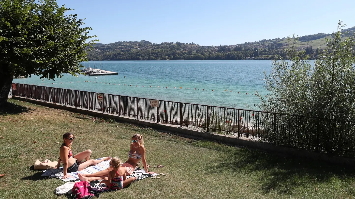 vue sur la plage du pin partie herborée avec une famille prenant un bain de soleil sur leurs serviettes, grand ciel bleu et vue sur le lac de paladru