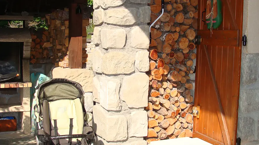 Vue d'une terrasse extérieure, stock de bois, abri de jardin avec cheminée d'extérieur pour barbecue, poussette bébé, table d'extérieur