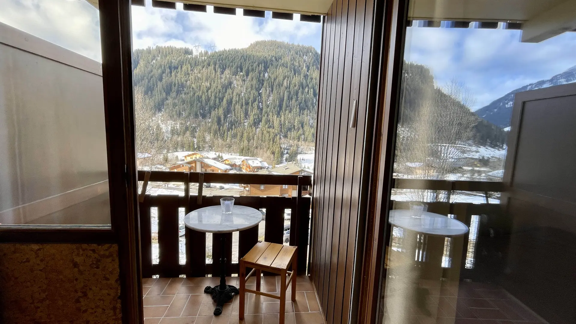 Vue sur le petit balcon depuis l'intérieur de l'appartement, table, chaise et Mt de Grange en arrière plan