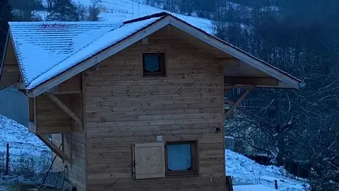 La cabane/chalet vue de l'extérieur l'hiver avec de la neige sur le toit et autour du chalet.