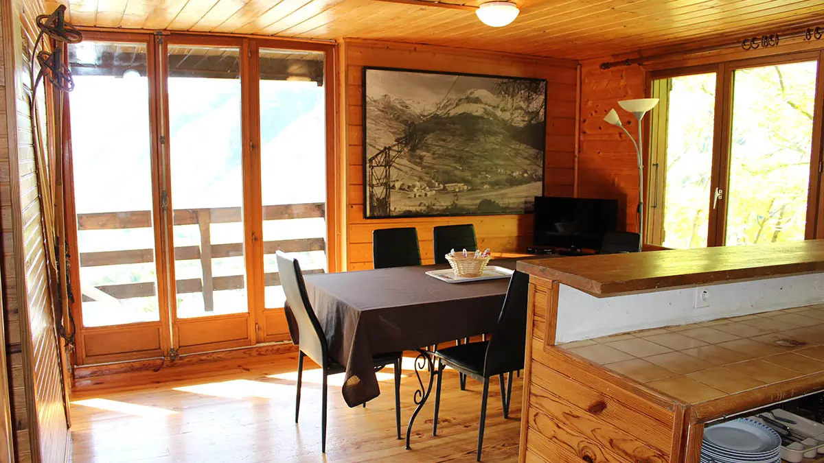 Séjour lumineux avec table à manger, bar, TV, ameublement bois, parquet au sol, fenêtre