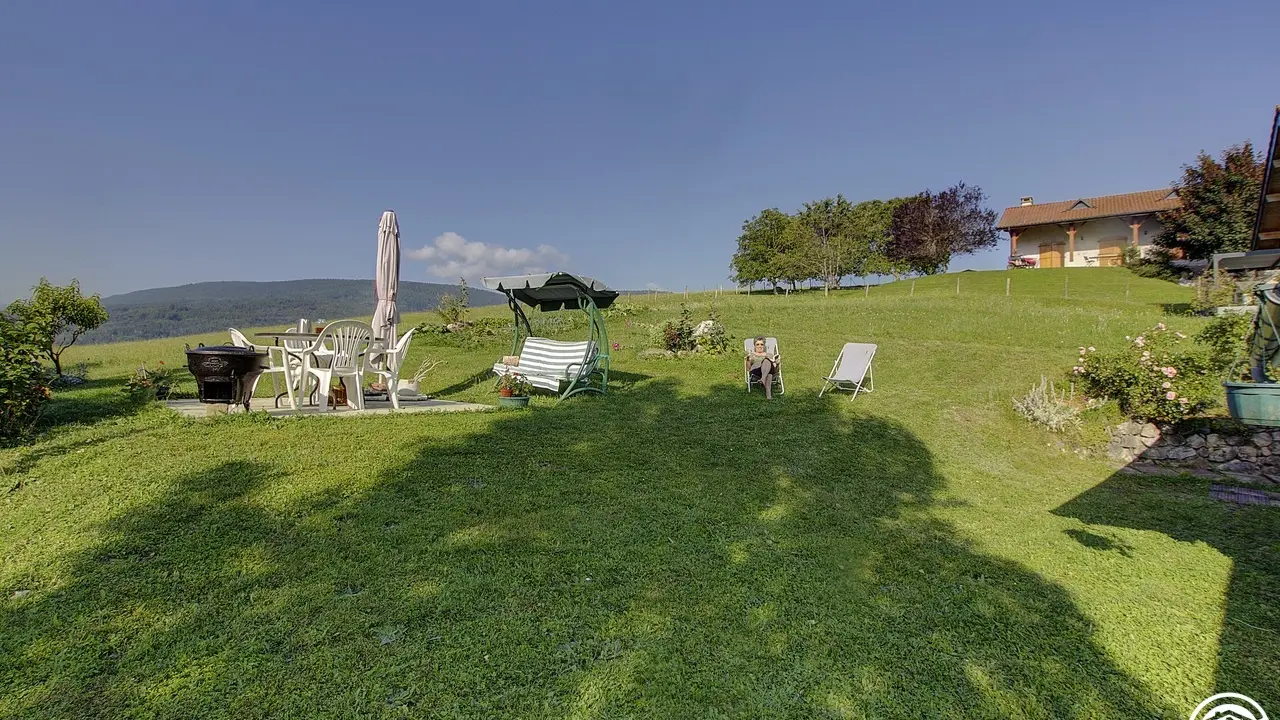 Vue prise depuis la maison sur le jardin avec une petite terrasse et des transats.
