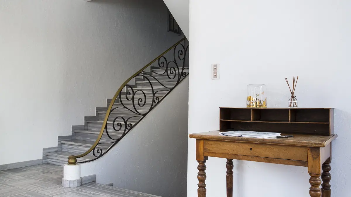 Hall avec un joli bureau ancien en bois, menant aux chambres via un escalier avec un rampe en fer forgé doré.