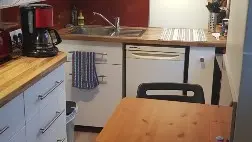 Cette cuisine compacte est équipée d'un plan de travail en bois, de placards blancs et d'une table rabattable et deux chaises pliantes.