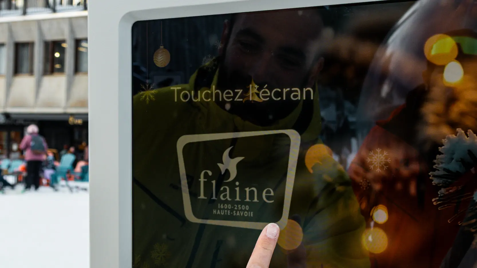 Une personne vêtue d'une veste jaune touche l'écran d'un photobooth installé en extérieur dans la neige.
