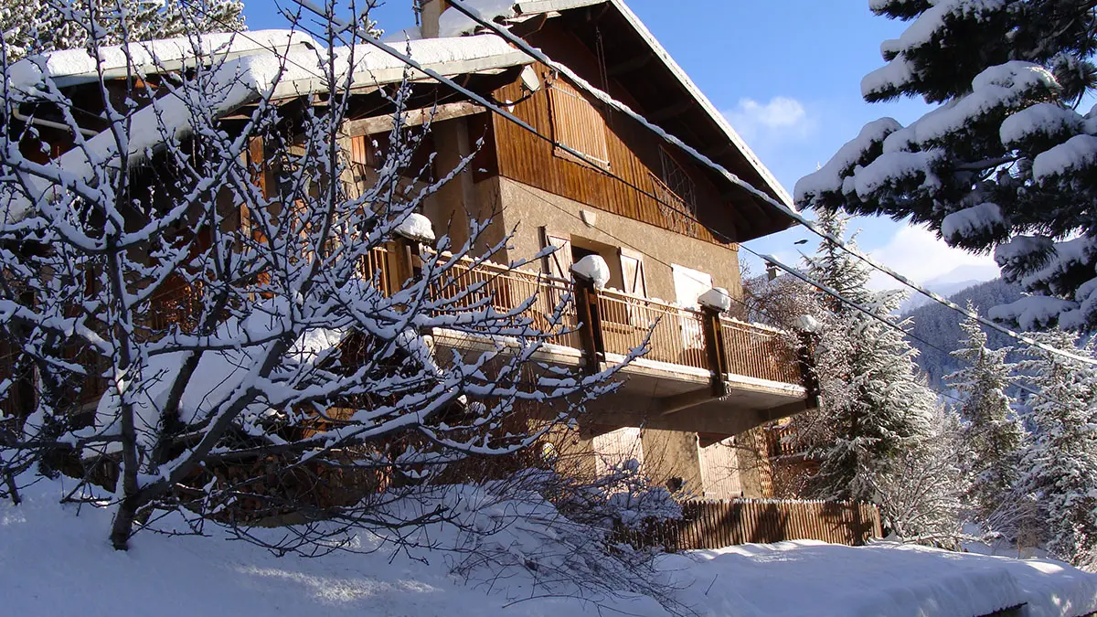 Vue de côté d'une maison en pierre et bois à trois étages, balcons métalliques, paysage hivernal enneigé