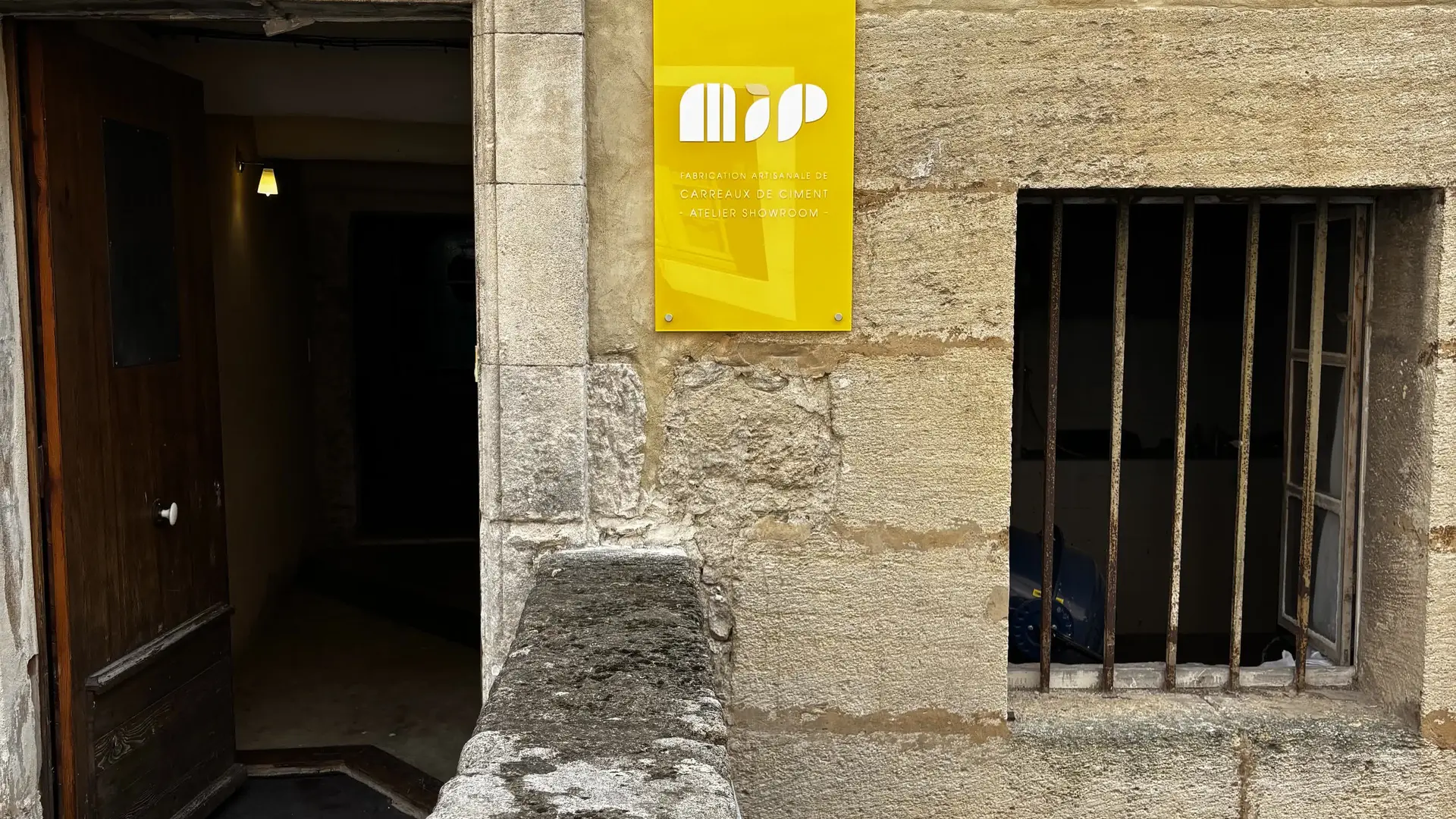 Façade ancienne et panneau jaune de l’Atelier MIP, créateur artisanal de carreaux de ciment.
