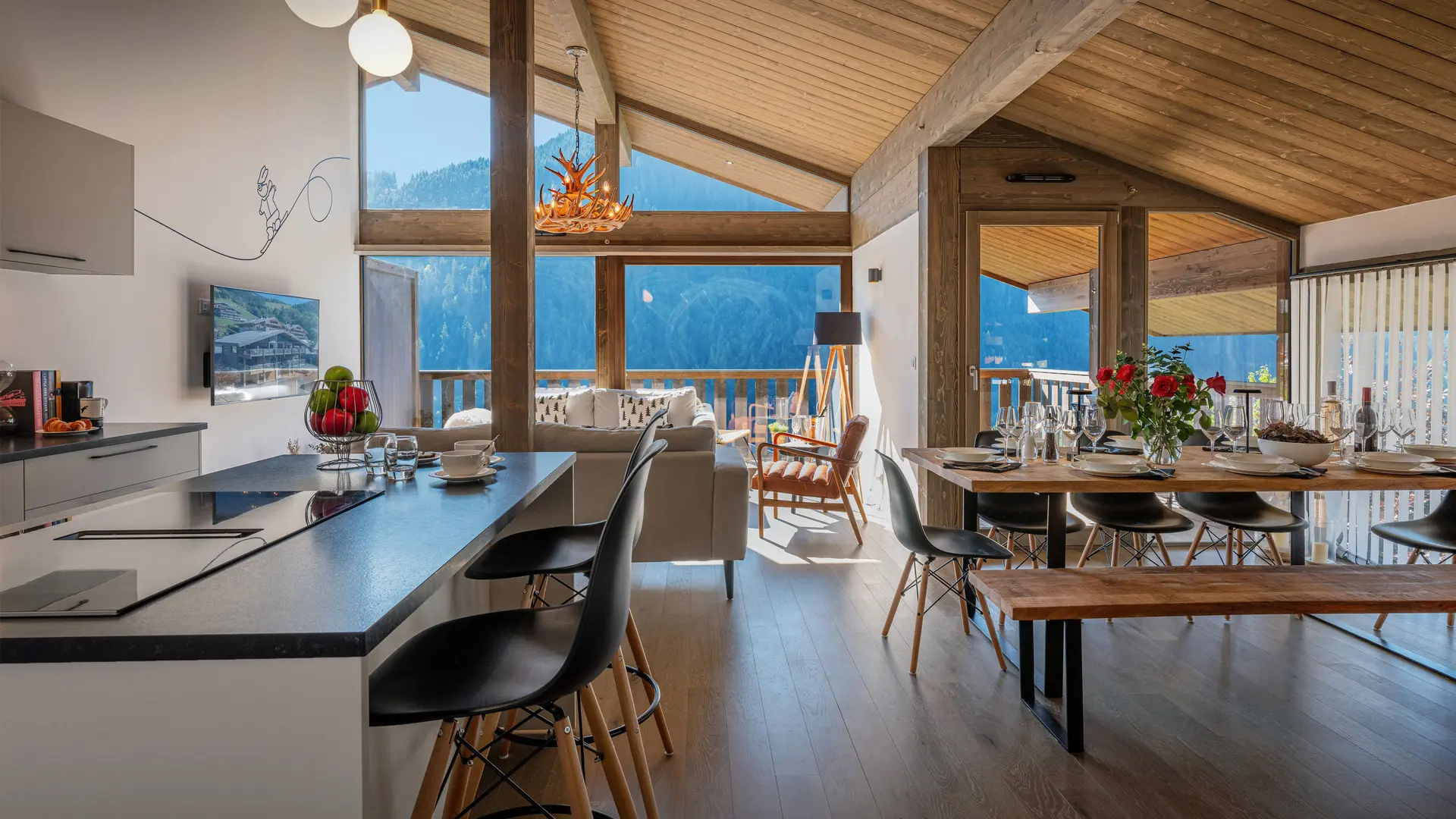 Vue d'ensemble de la pièce à vivre avec cuisine, salle à manger et salon, grandes baies vitrées donnant accès au balcon avec vue sur les montagnes