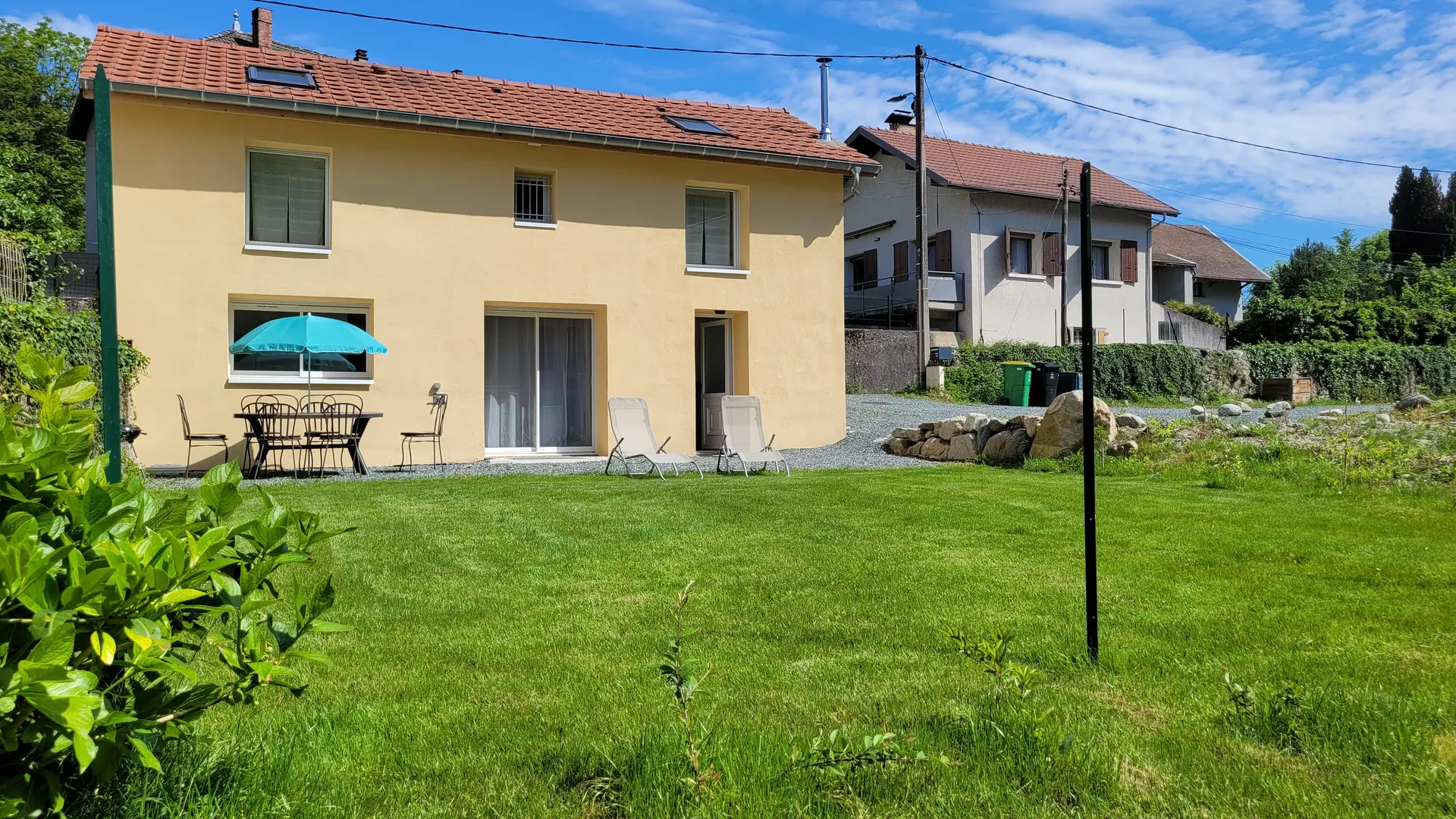 Il s'agit d'une maison individuelle avec une façade jaune et un terrain extérieur spacieux. Le jardin est principalement composé de pelouse, avec quelques arbres en arrière-plan.