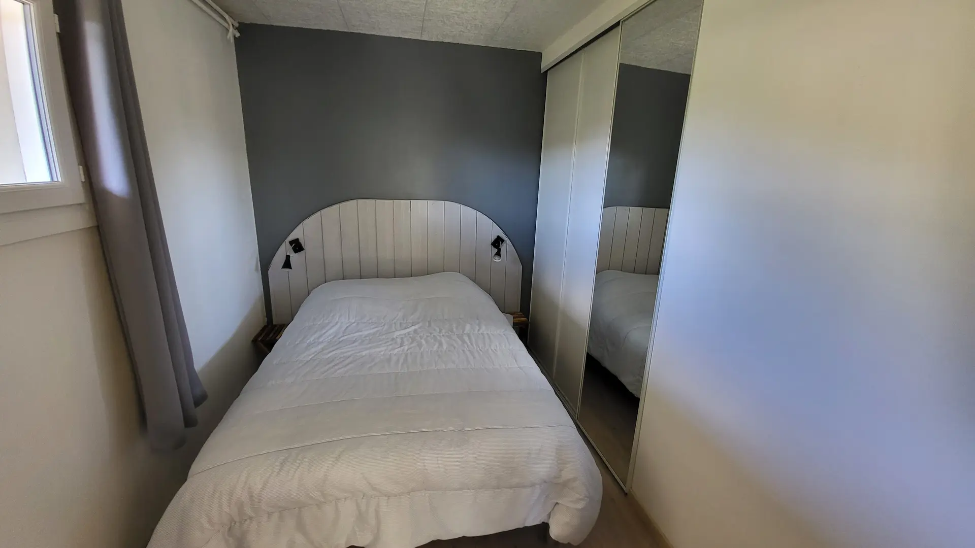 Cette chambre contient un lit double avec une tête de lit en bois, un grand placard mural avec un miroir.