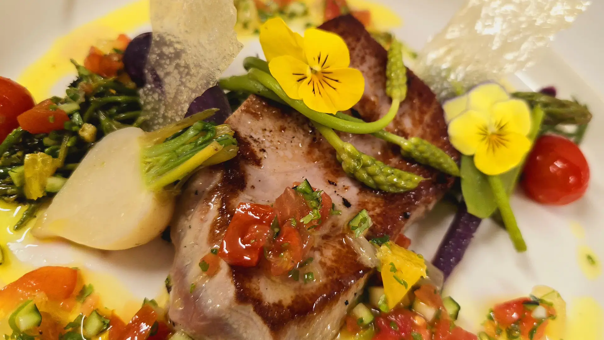 Une assiette colorée et élégante où se mêlent poisson, légumes frais et fleurs comestibles.