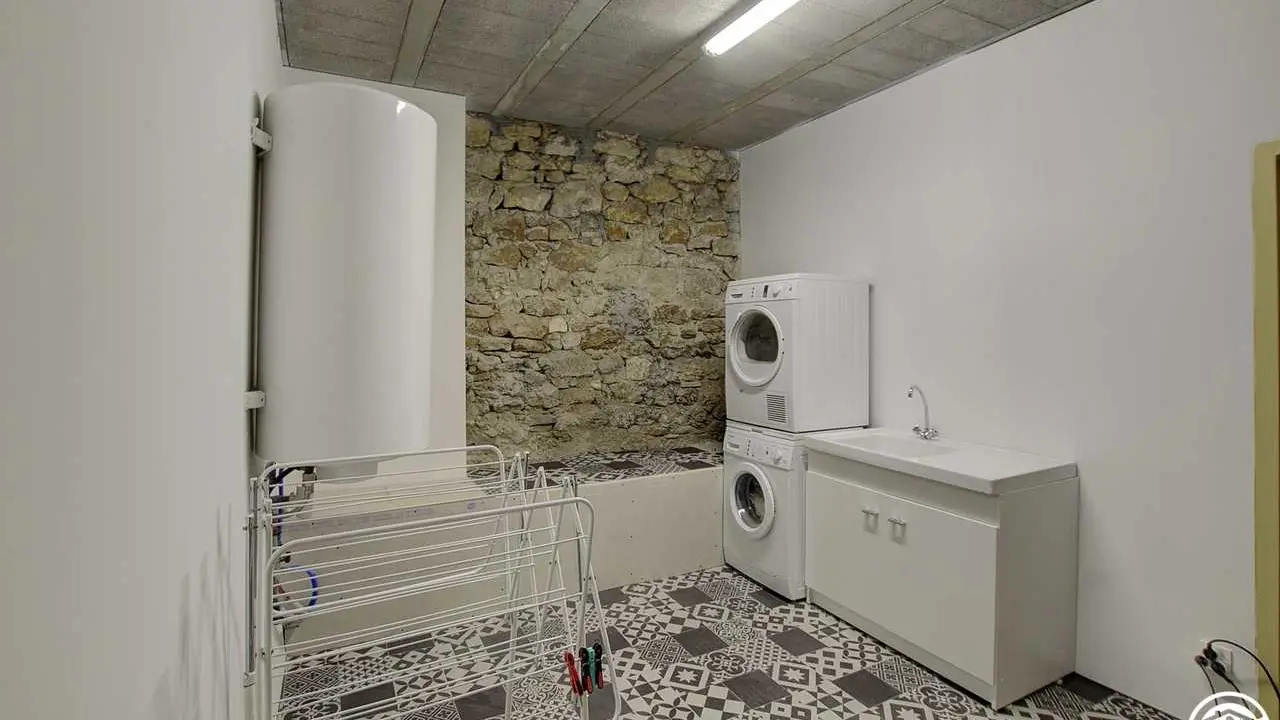 Une grande buanderie avec lave-linge  sèche-linge table à repasser et un point eau