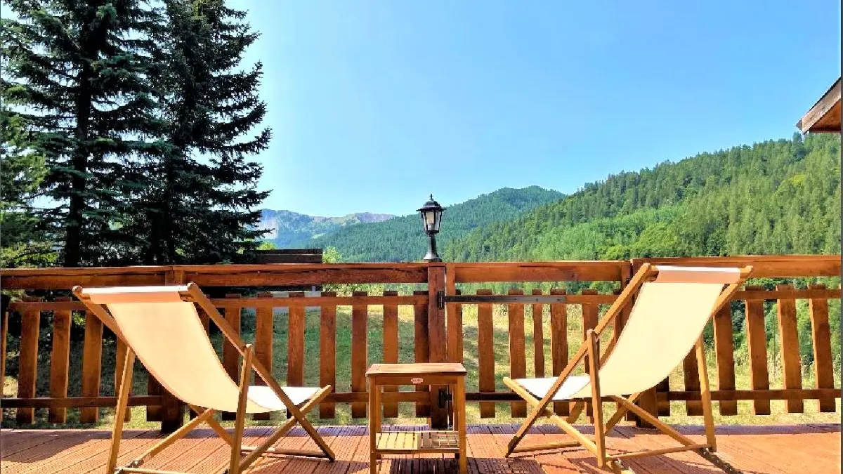 Terrasse en bois du chalet avec transat, vue dégagée avec paysage d'été