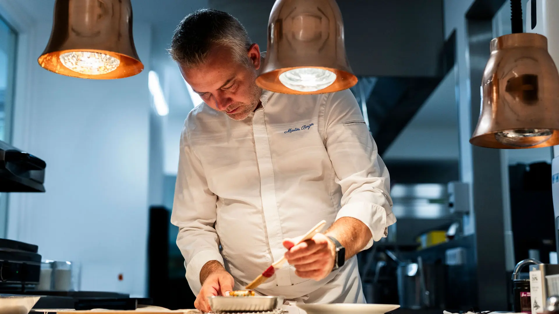 Portrait de Martin Berger, chef de la Table d'Uriage, dressant un plat dans sa cuisine.