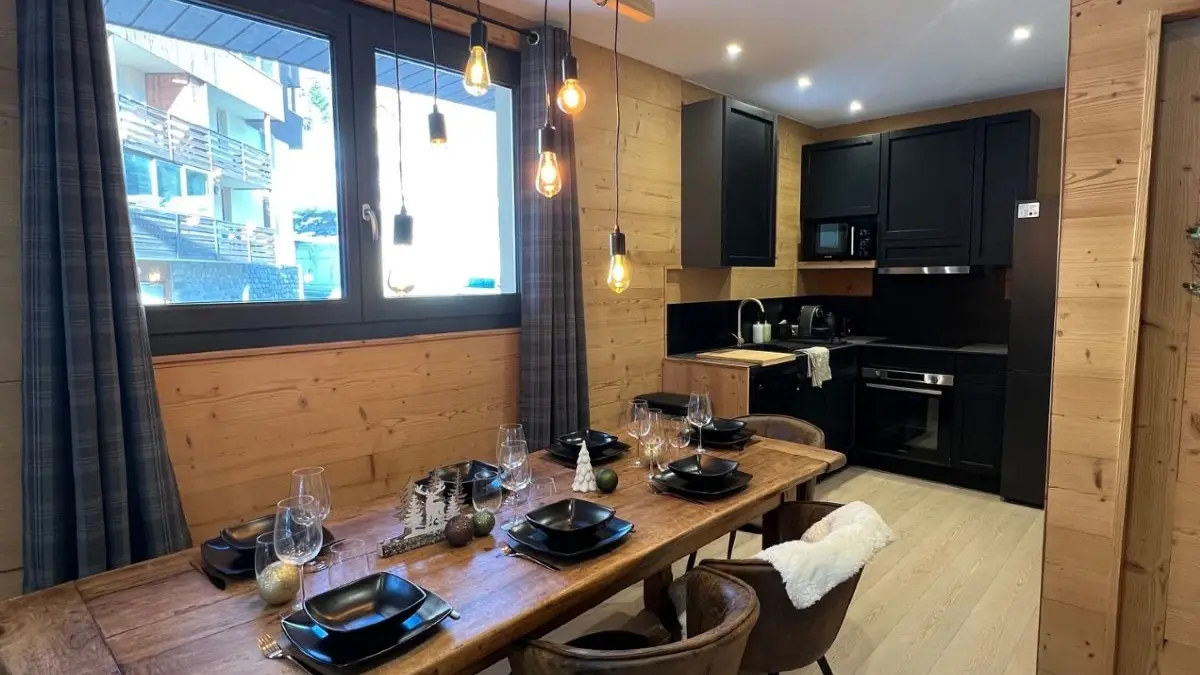 Bright living room with large dining table, modern kitchen area, wooden interior furniture, windows opening outside