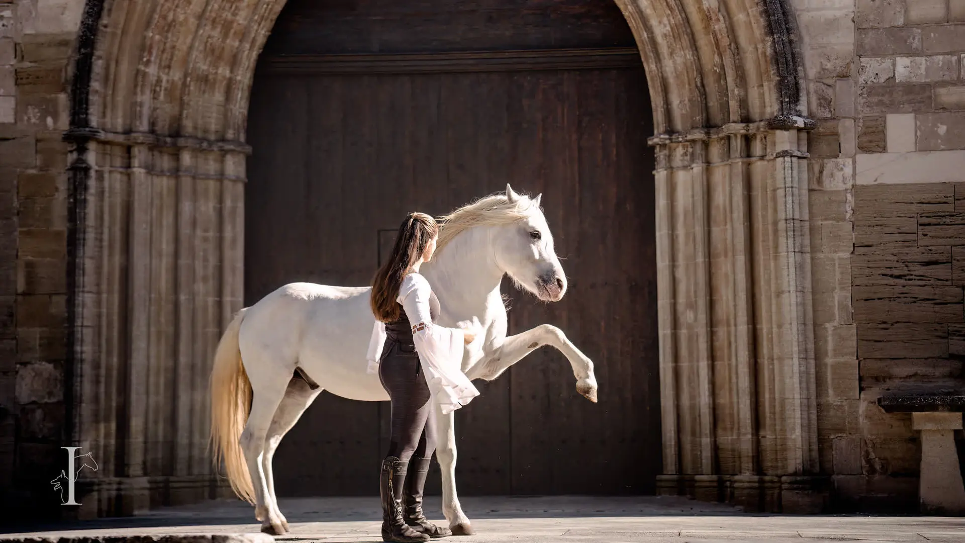 Photo artistique d’une cavalière et de son cheval devant un portail ancien.