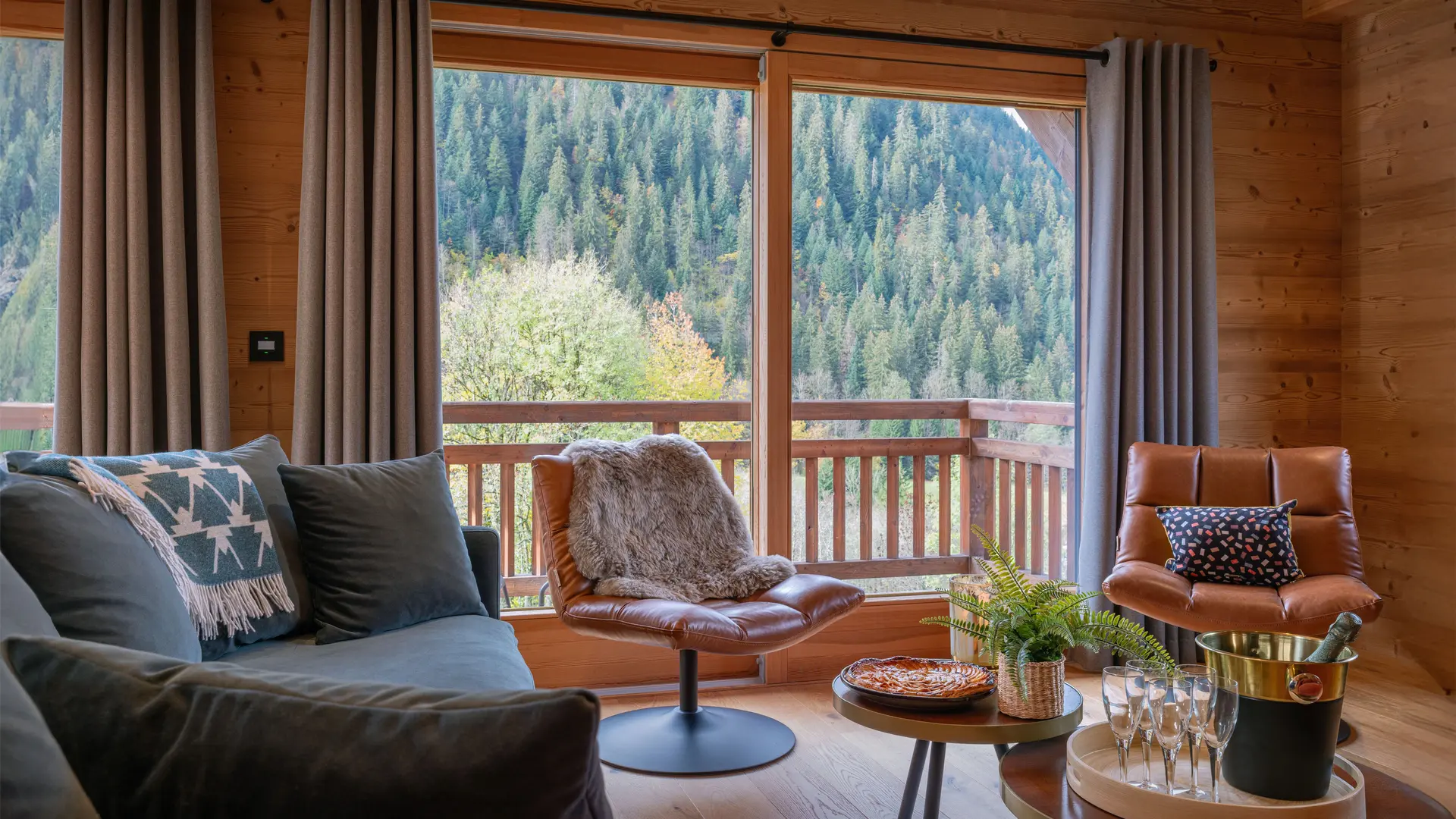 Salon avec ses canapés, fauteuils et grande baie vitrée donnant accès au balcon et vue sur les montagnes
