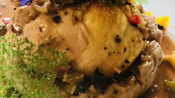 Plat chaud pintade sur un lit de légumes avec sa sauce. Elle est accompagnée de dentelle de légumes et de fleurs comestibles.