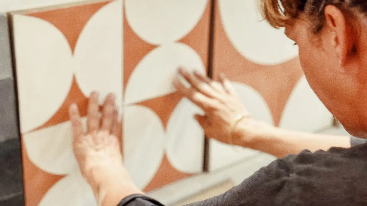 Artisane positionnant soigneusement des carreaux de ciment aux motifs géométriques.