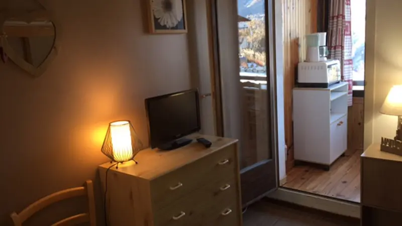Studio apartment living room with TV, wooden furniture, French doors opening onto an additional room