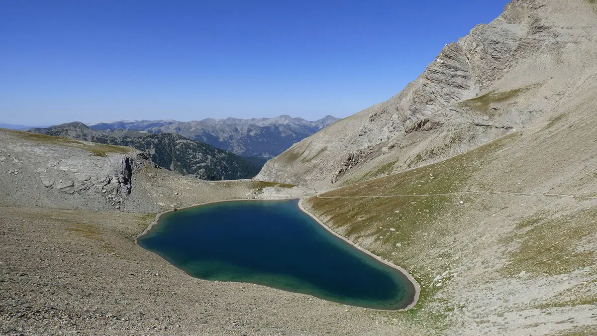 Lake Cayolle, a large body of water set amidst a rocky promontory with sparse vegetation. Mountains in the background