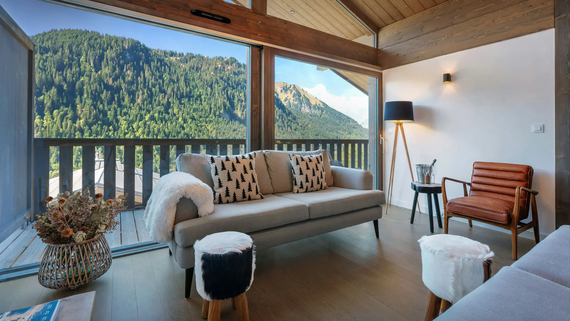 Salon très lumineux avec canapé et fauteuil, grande baie vitrée donnant accès au balcon et vue sur les montagnes