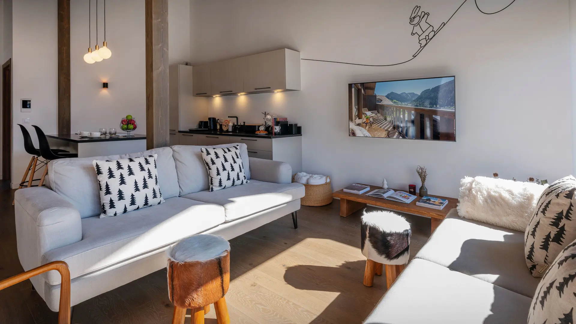 Salon avec ses deux canapés, fauteuil et pouf, cuisine en arrière plan