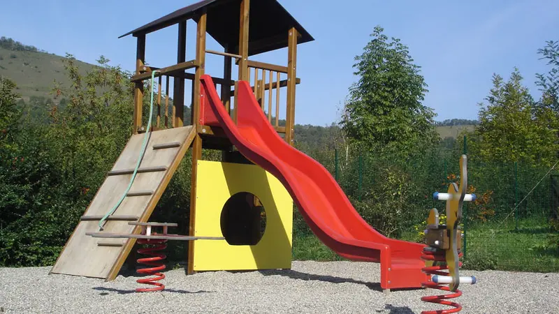 L'aire de jeux est composée d'un portique en bois avec un toboggan rouge, accessible par une échelle en bois et un tunnel jaune.