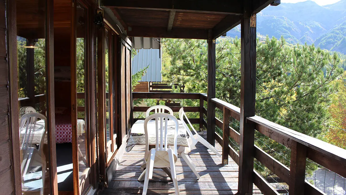 Balcon en bois ensoleillé avec table et chaises, vue sur les montagnes