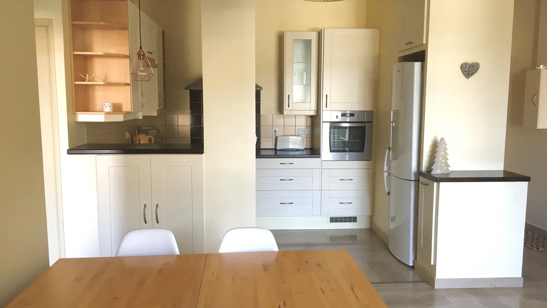 Cette pièce à vivre se compose d'un espace salle à manger avec une table et des chaises, et s'ouvre sur une cuisine fonctionnelle dotée d’un four et d’un grand frigo.