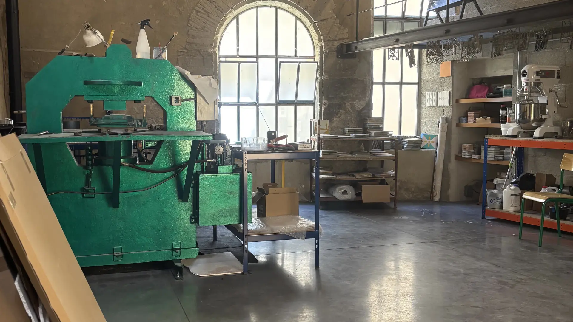 Salle de fabrication bénéficiant de grandes fenêtres, machines et établis dédiés aux carreaux de ciment.