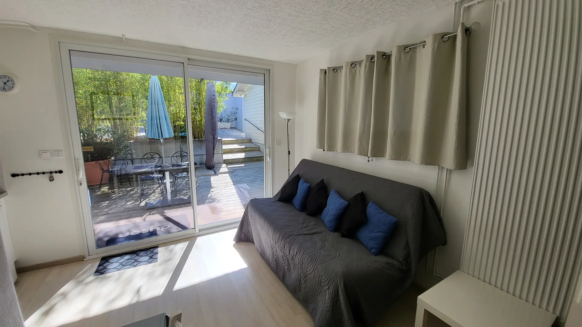 Cet espace est une pièce avec un canapé sur la droite, une table et des chaises sur la gauche, et une grande ouverture sur l'extérieur en face.